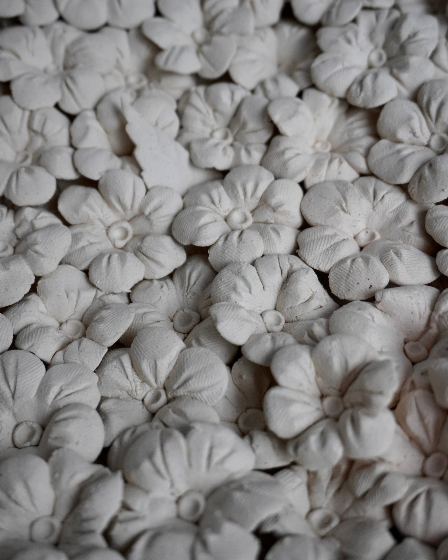Close-up of white ceramic flowers arranged in a pattern. you can see the fingerprints that pressed into the clay. the flowers are 6 petals with two lines going up the petal. the middle is a ball with a pressed in middle.