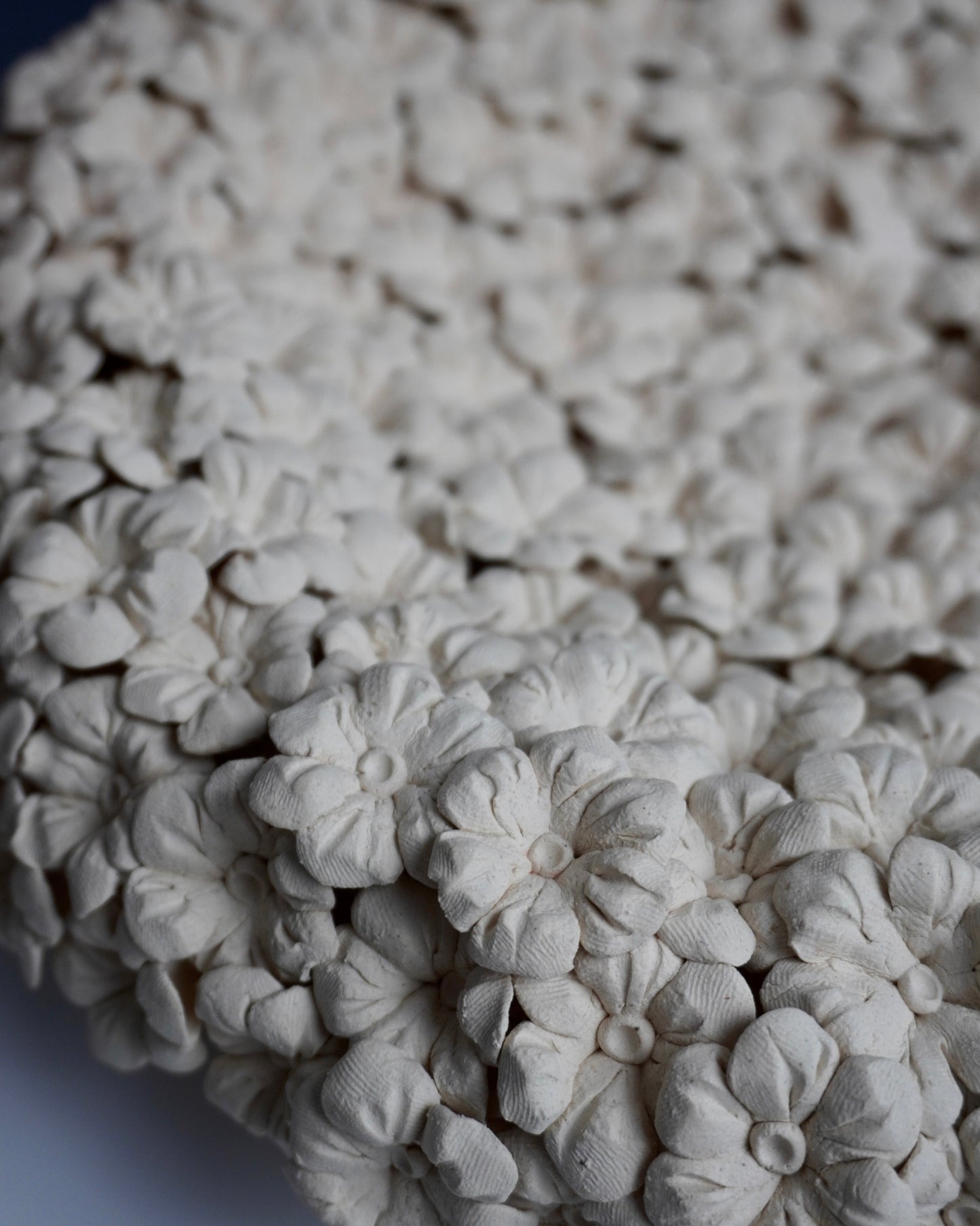 Close-up of white ceramic flower-shaped objects on a textured surface.you can see the fingerprints that pressed into the clay. the flowers are 6 petals with two lines going up the petal. the middle is a ball with a pressed in middle.