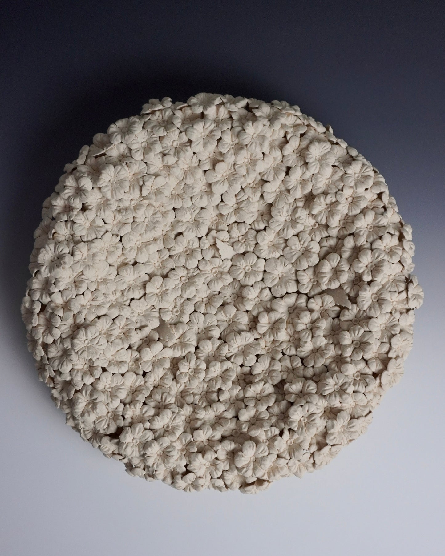 ceramic art piece with and pinched flowers. circular with the inside sunken in. the flowers cover the whole piece