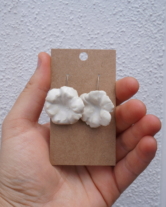 Hand holding a card with white floral earrings against a plain background