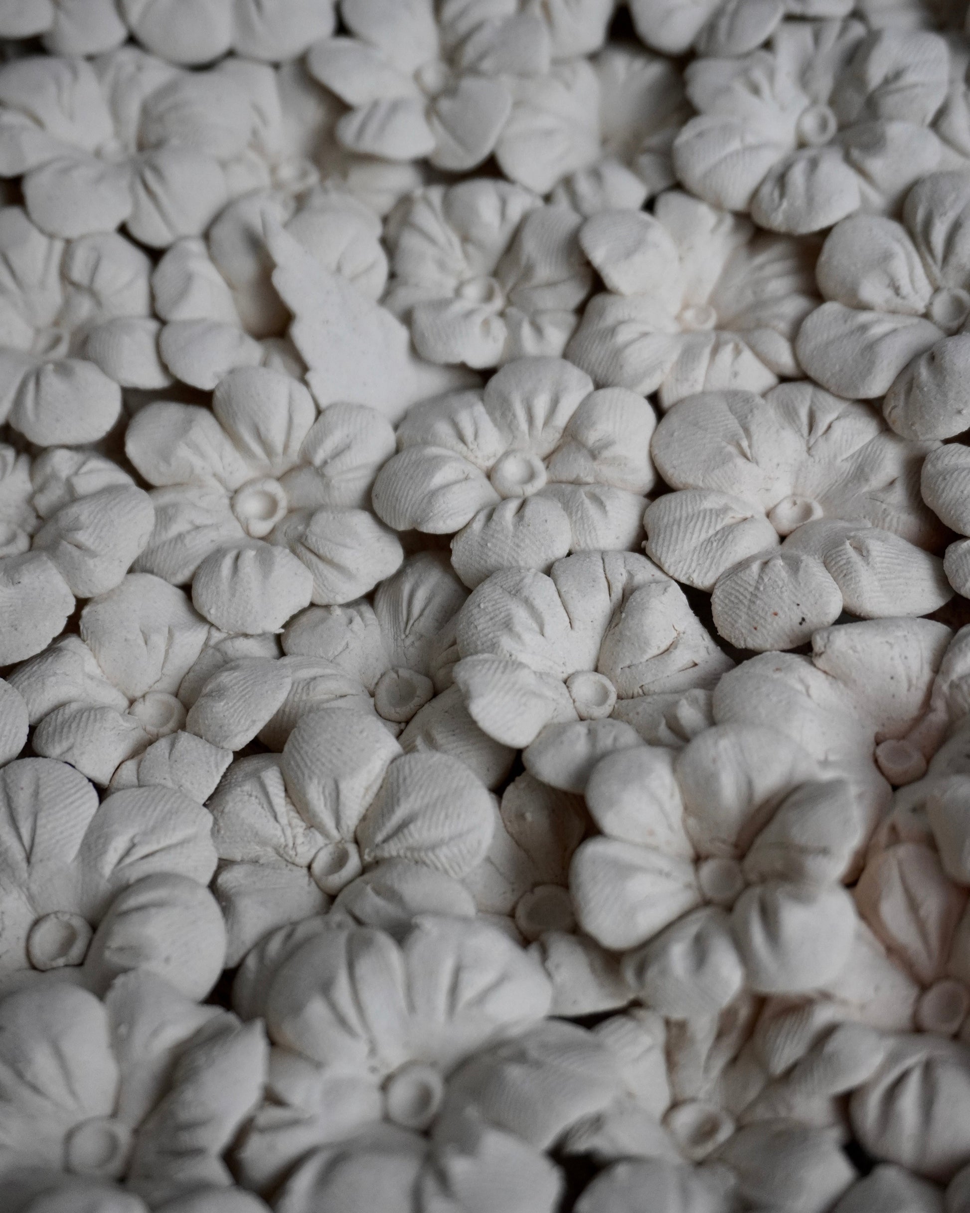 Close-up of white ceramic flowers arranged in a pattern. you can see the fingerprints that pressed into the clay. the flowers are 6 petals with two lines going up the petal. the middle is a ball with a pressed in middle.