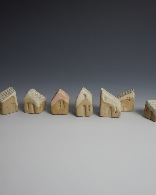 A row of small hand-carved wooden house figurines in natural beige wood, arranged on a light gray surface against a dark gray gradient background.