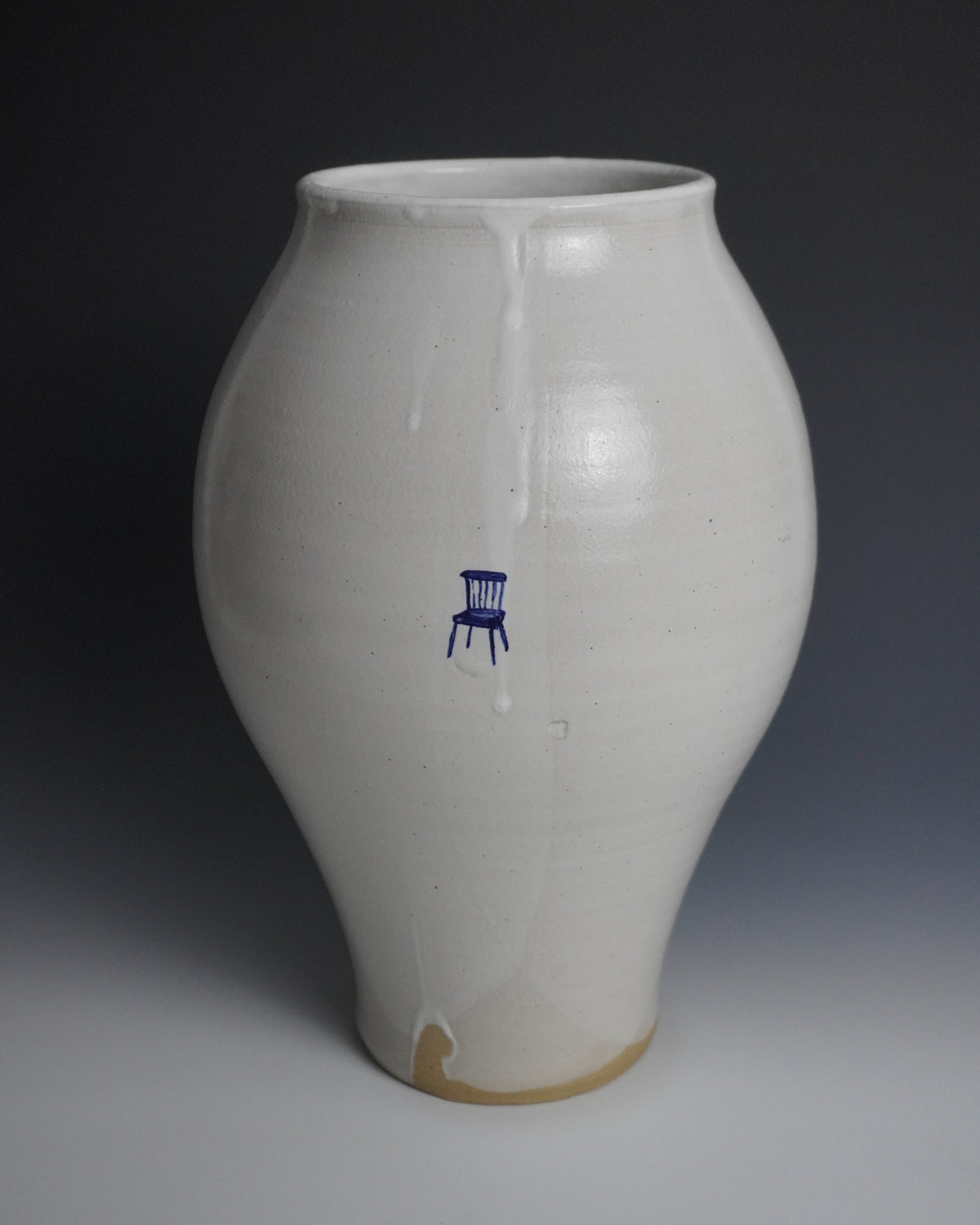 A handmade ceramic vase with a rounded bulbous body, a glossy off-white glaze, and a small blue chair motif on the front, set against a dark gray gradient background.