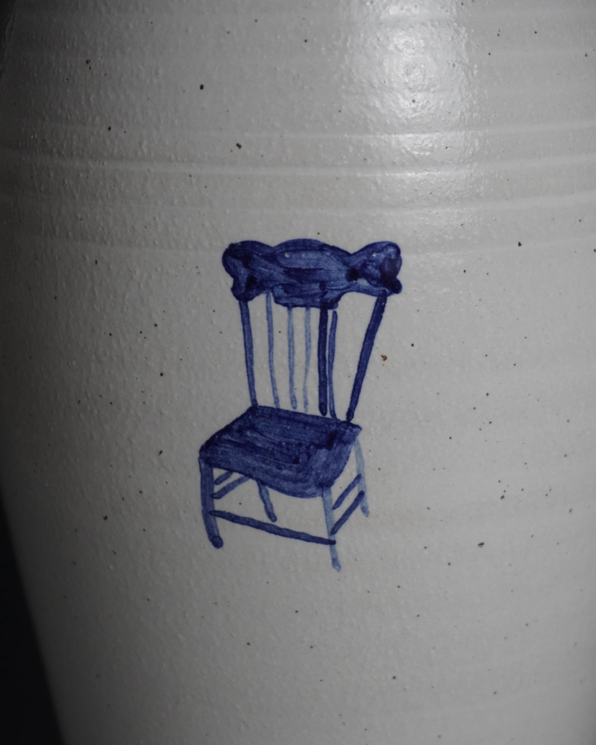 A close-up of a white speckled ceramic surface featuring a hand-painted blue illustration of a wooden chair.
