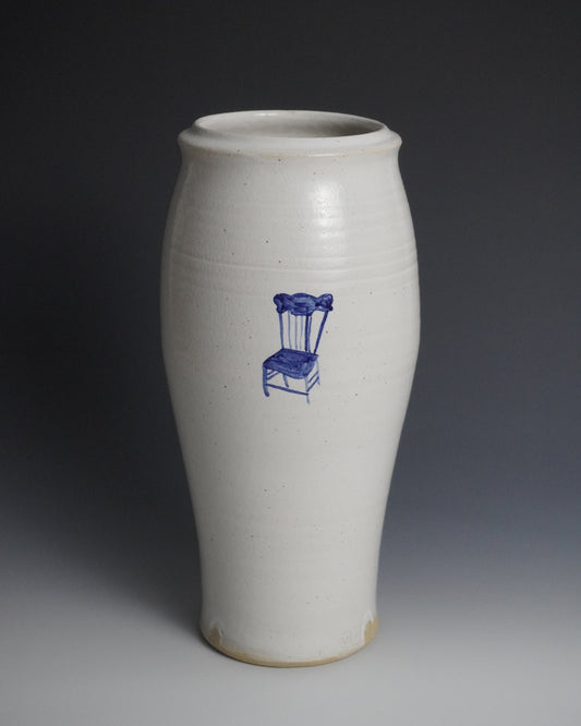 A tall, white ceramic vase with a blue line drawing of a chair on the front, set against a dark gray gradient background.