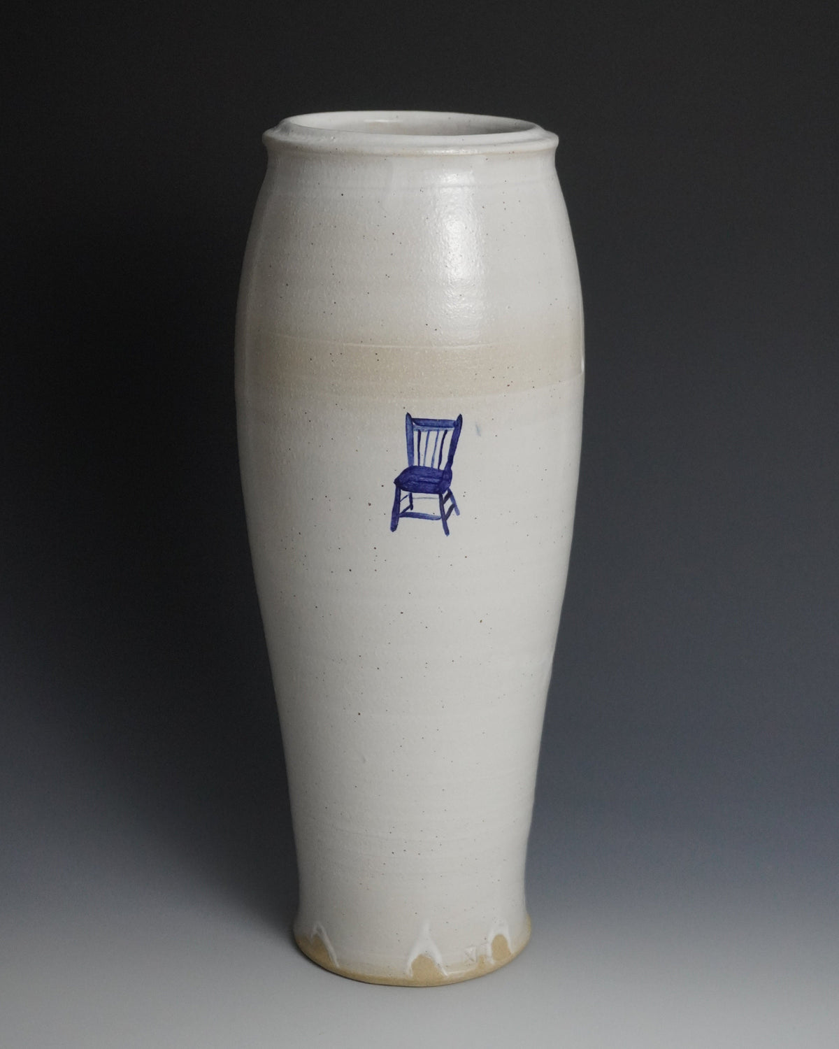 A tall, flared ceramic vase with a glossy off-white glaze and a small blue chair illustration on the front, set against a dark gray gradient background.